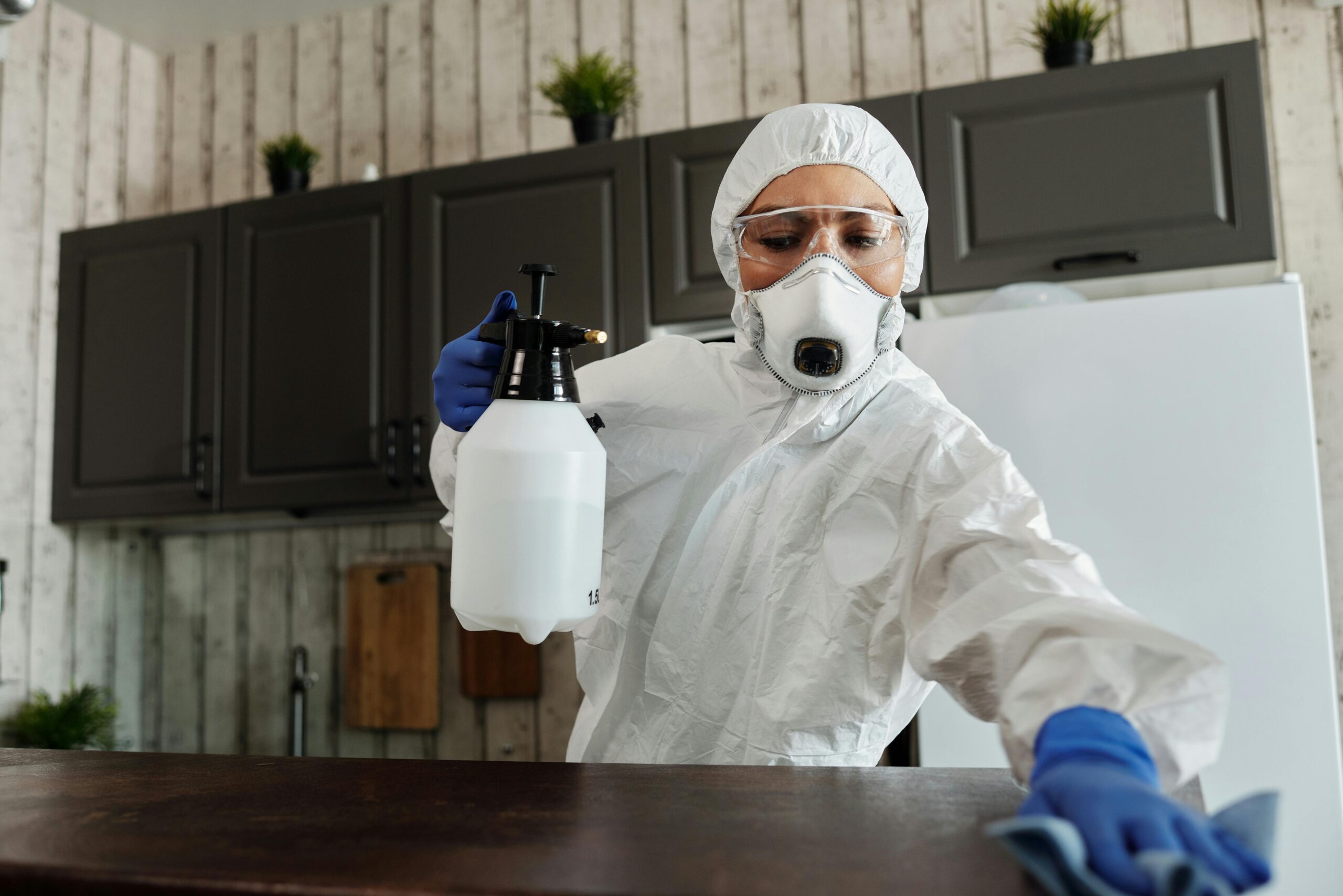 pexels-photo-4099462-4099462 A woman in protective gear disinfecting an indoor area using a spray bottle.